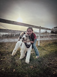 a little girl hugging a white dog in front of a fence