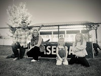 a black and white photo of a family posing in front of a baseball sign