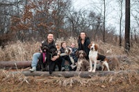 a family poses with their dogs on a log in the woods