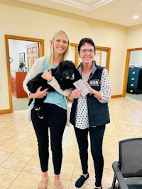 two women standing in an office with a black dog