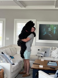 a man is hugging a large black dog in a living room