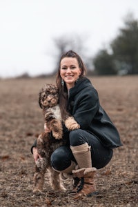 a woman kneeling down with a dog in a field