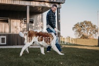 a man walking his dog in front of a barn