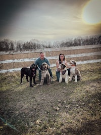 a man and woman pose with their dogs in front of a fence