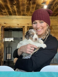 a woman holding a puppy in a barn