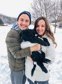 a man and woman holding a black dog in the snow