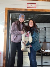 two women standing next to a dog in a kennel