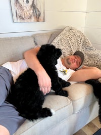 a man laying on a couch with two black dogs