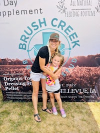 a woman and a little girl posing in front of a brush creek sign